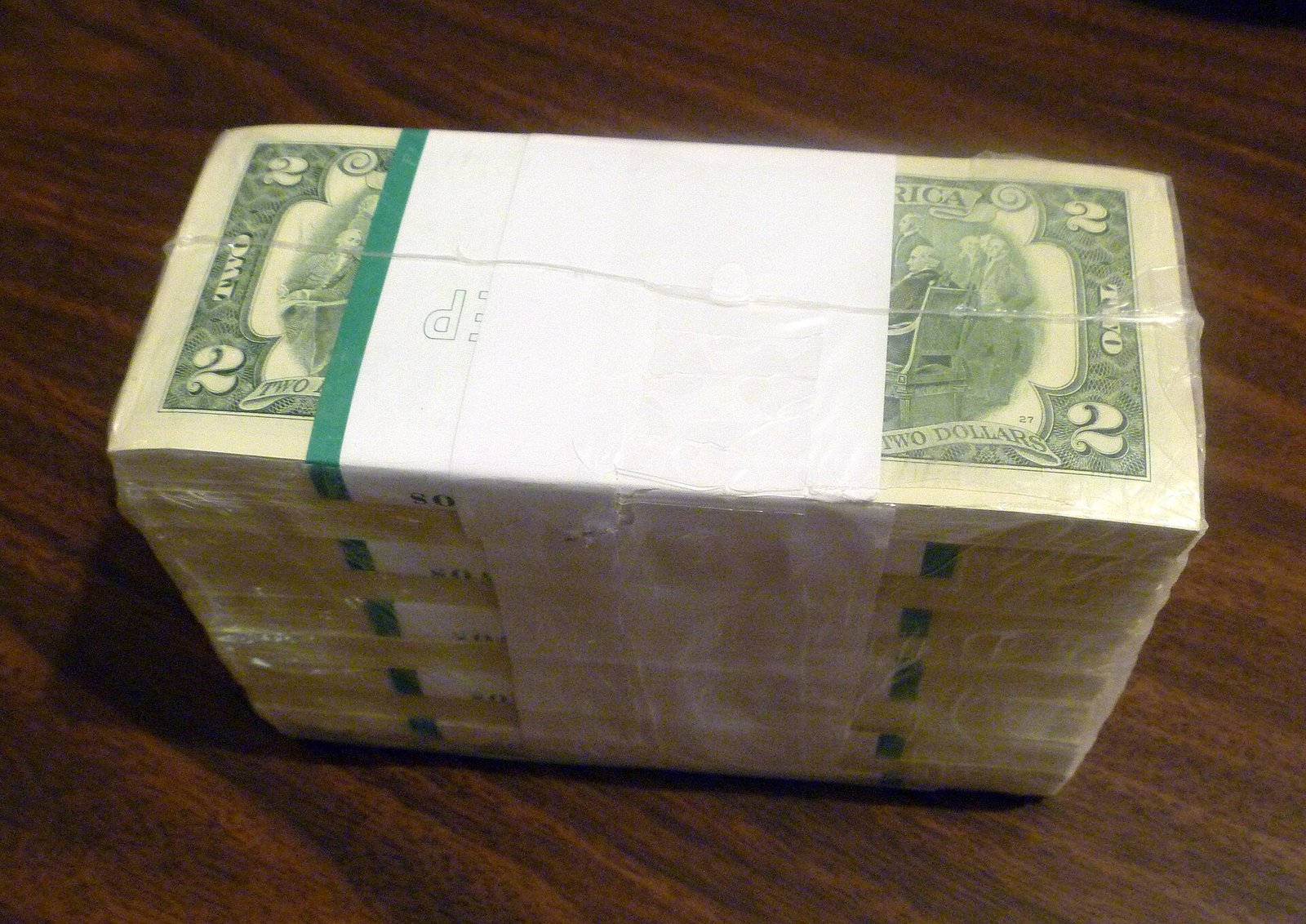 A shrink-wrapped brick of one thousand two-dollar bills with green straps