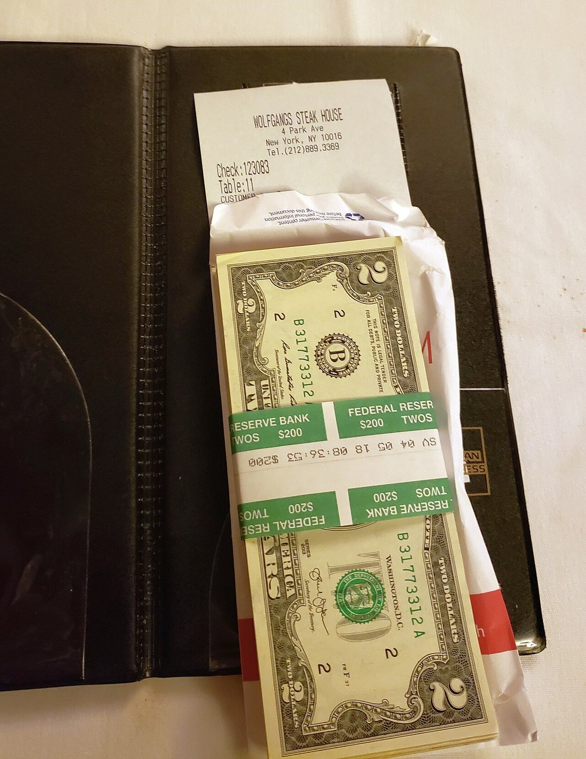 A stack of one hundred two-dollar bills tucked into a restaurant check presenter